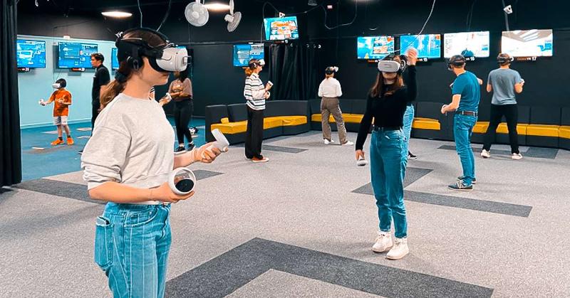 Plusieurs jeunes dans une grande salle avec des casques et manettes de jeux de réalité virtuelle lors du voyage linguistique angleterre