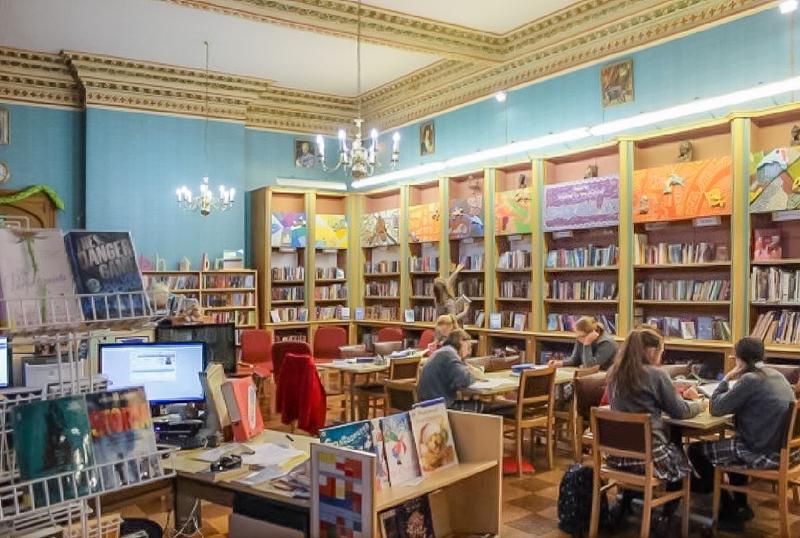 Bibliothèque du voyage linguistique angleterre avec des étagères de livres et des enfants à des tables en train de lire ou travailler