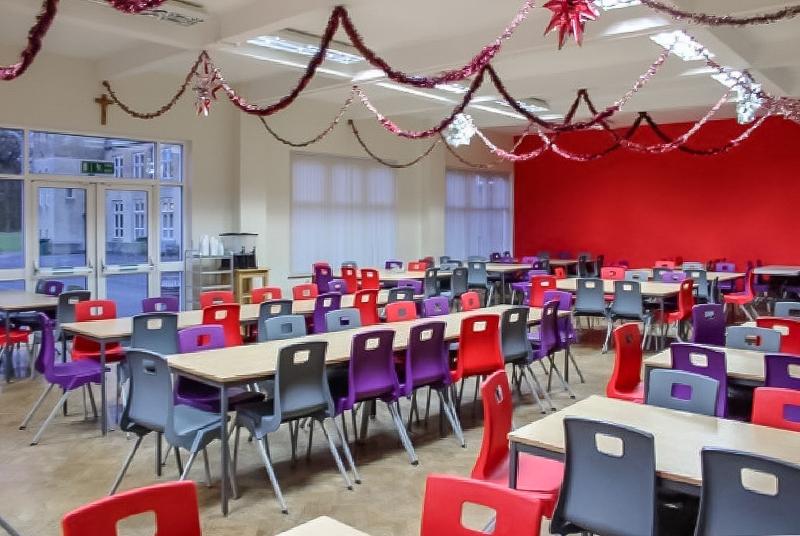 Grande salle du voyage linguistique angleterre avec des grandes tables et des chaises colorées il y des guirlandes au plafond 