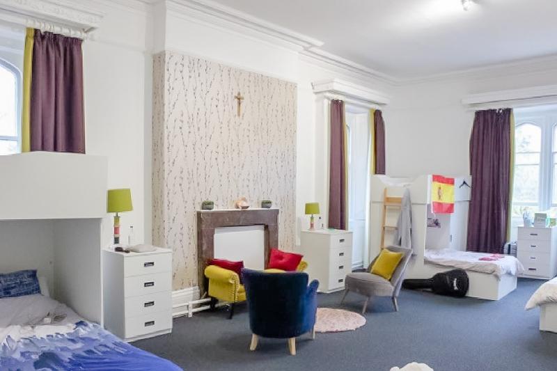Grande chambre du voyage linguistique angleterre avec plusieurs lits et un coin salon avec fauteuils, tapis et coussins