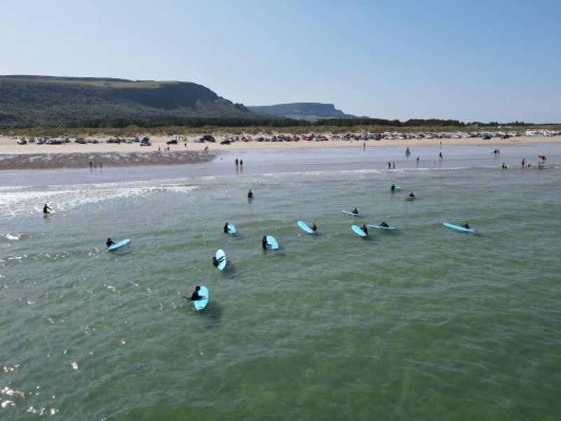 Vue du ciel de la plage avec des enfants du séjour linguistique irlande dans l'eau avec leurs planches de surf 