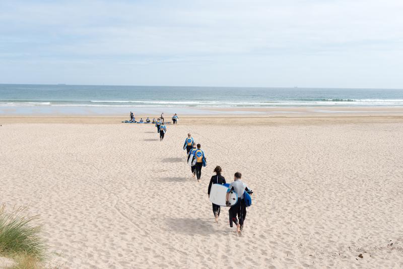 jeunes pôrtant des planches de surf sur le sable pour aller jusqu'à la mer en séjour linguistique irlande 