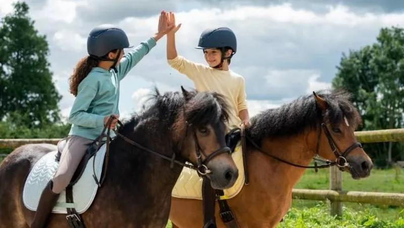 Enfants sur des poneys qui se tapent dans les mains en colonie de vacances Metz