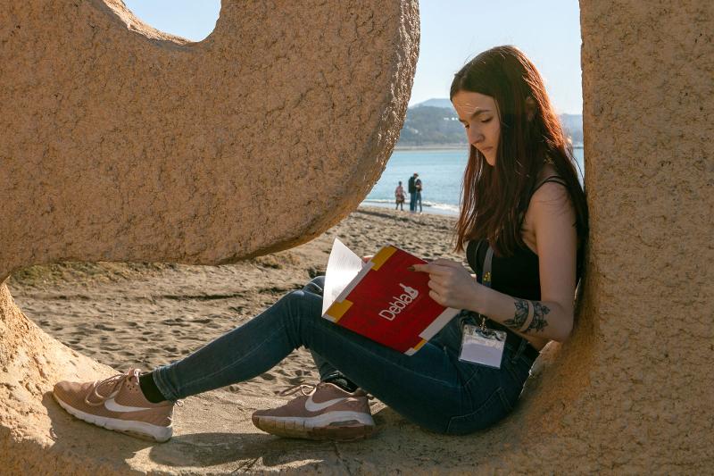 Jeune fille lit livre espagnol assise contre une pierre