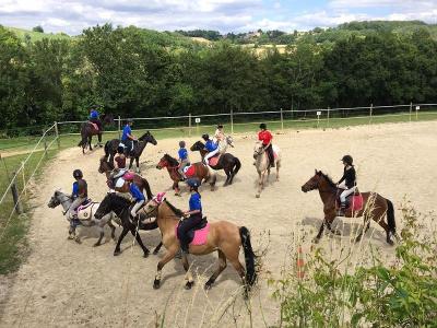 Un groupe de cavaliers effectuent des exercices avec leur chevaux dans un manège en extérieur lors de la colonie de vacances d'équitation