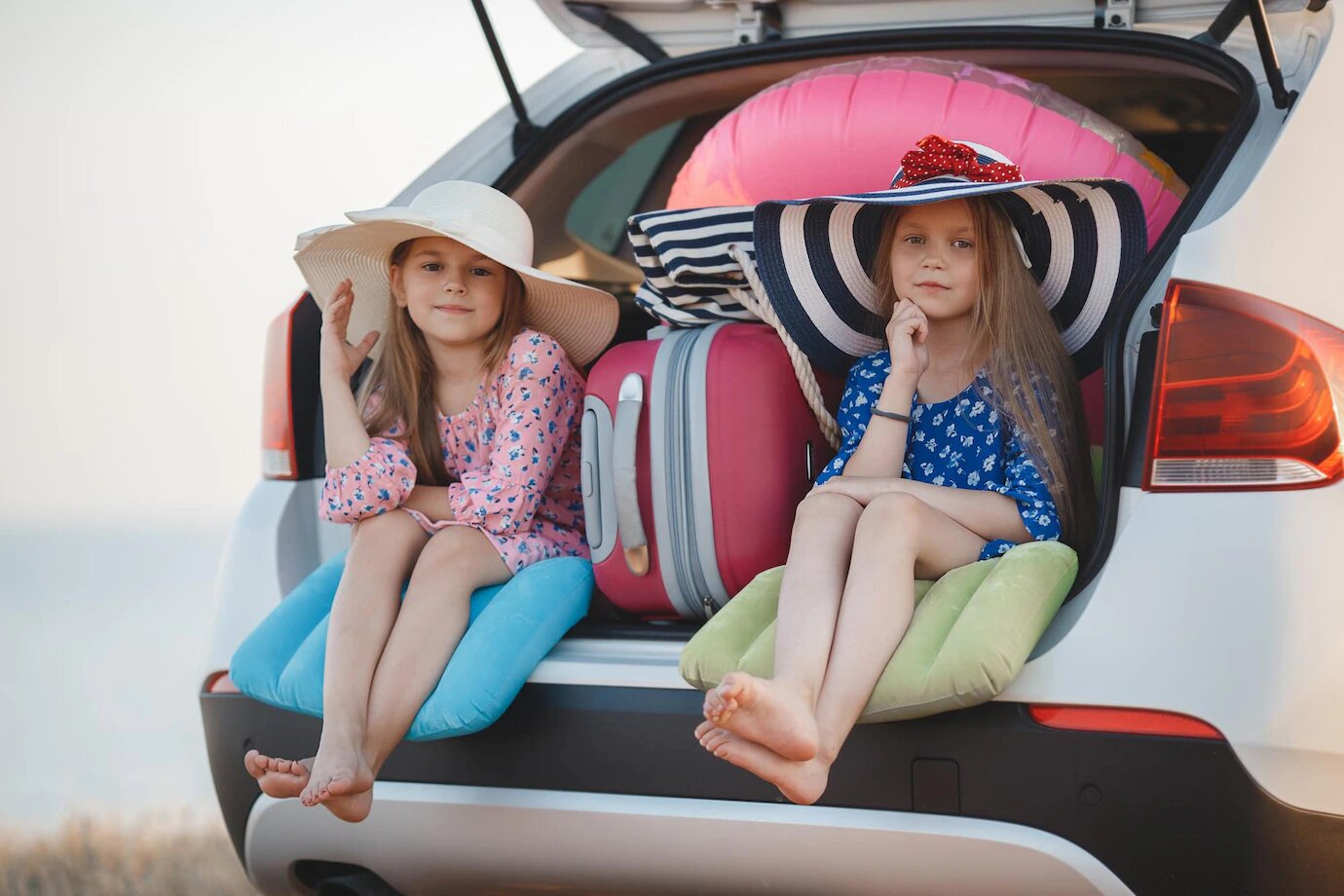 deux petites filles assises au bord du coffre de la voiture prêtes à voyager avec leur valise