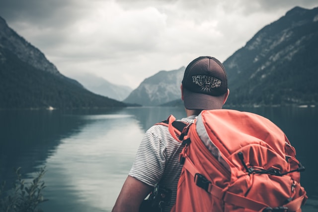 jeune de dos avec un sac à dos devant un lac et des montagnes